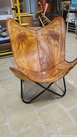 Front view showing detailed hand carved leather with animal motifs on a vintage butterfly chair with black steel base.