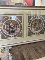 Framed fine art depicting two circular classical prints with seated figures and cherubs, in silver-tone frame with matting.
