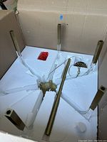 Chandelier components nestled in custom foam insert inside original cardboard box, showing six brass-finish iron arms and clear acrylic rods.
