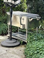 Full view of stainless steel rolling ice chest cart outdoors, showing large side handles and wheels.