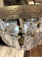 Close-up view of embossed floral and rope detail metal frame section with hanging faceted crystal prisms of one chandelier.