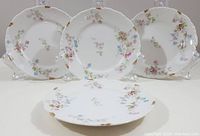 Four antique C. Ahrenfeldt Limoges side plates displayed with one lying flat and three standing, showing floral and gold edge details.