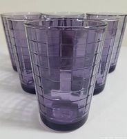 Front view of several purple patterned glasses arranged together showing the textured rectangular pattern and translucency.
