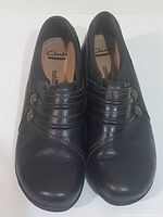 Top view of both shoes, showing brown leather uppers with elasticized ribbed detailing and decorative metal buttons. Round toe shape visible.
