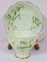 Front view of tea cup and saucer with visible snowdrop floral design, set on wooden stand