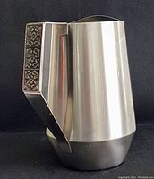 Front angled view showing brushed stainless steel surface and decorated handle with floral panels.