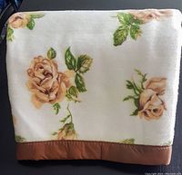 Folded view of the vintage Texmade blanket showing yellow rose pattern and brown border on white background.