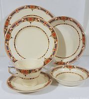 Full set of one place setting with all six pieces displayed: dinner plate, salad plate, side plate, cereal bowl, nappie, cup and saucer. Highlights Art Deco pattern with floral and geometric design on cream porcelain.
