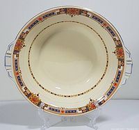 Full front view of the oval serving bowl showing the intricate Art Deco floral and geometric border design with dual handles and cream interior.