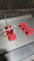 Three red spring-loaded pipe clamp fittings and three fixed base pipe clamp fittings placed on a metal surface.