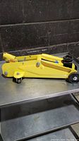 Side view of yellow hydraulic trolley jack in lowered position on metal table with black wall background