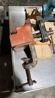 Small red clamp-on vise showing clamp mechanism and worn orange paint