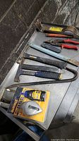 Overview of demo tools laid on metal surface showing mostly hammers, chalk line kit in packaging, and pry bars.