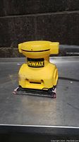 Front view of yellow DeWalt palm grip sander showing logo and sanding pad with used sandpaper.