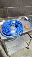 Blue extra heavy duty extension cord coiled on metal cart, showing full length of cord with connectors visible