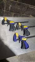 Three used Irwin Quick-Grip bar clamps with yellow trigger for one-handed clamping on a metal surface.