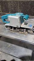 Side view of Makita belt sander showing overall body, handle, and sanding belt system.