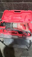 Full view of Milwaukee sawzall inside red carrying case on metal surface.