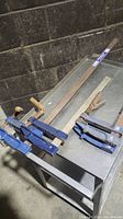 4 metal bar clamps of various lengths with blue handles on a metal table, showing overall look and sizes.