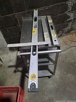 Three measuring tools laid on a metallic rolling cart: Stanley 4-foot level, Johnson 2-foot level, and Empire 2-foot framing square.