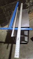 Photo showing the three measuring tools laid on a table: a blue T square, and two metal straight edge rules.