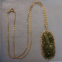 Full view of 14k gold chain and jade pendant laid flat on fabric background