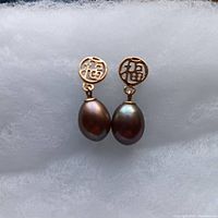 Front view of pair of 14K gold earrings with black teardrop-shaped black pearls and circular gold tops with cut-out design.