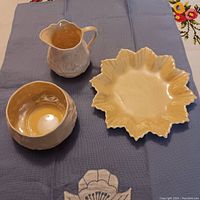 Full view of three cream Belleek porcelain pieces: pitcher, bowl, and leaf-shaped dish on a blue cloth