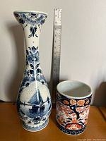 Delft blue and white vase and Japanese Imari brush pot side by side with ruler for scale.