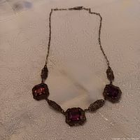 Full view of the antique sterling filigree necklace with three purple stones laid on a fabric surface.