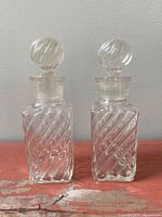 Pair of clear glass Art Deco perfume bottles with a diagonal bamboo twist pattern, square base and round stopper on top.