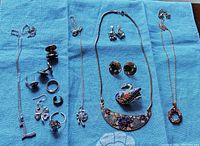 All items laid out on blue cloth showing entire lot with necklaces, brooch, rings, and earrings including marked 925 and Coro screwback earrings.