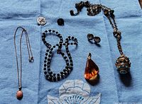 All items laid out on blue cloth showing variety of costume jewelry including necklaces, pendants, earrings, and beads.
