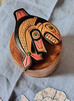 Top view showing the lidded wooden box with a carved and painted killer whale motif in black, red, and green colors.