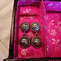 Front view of John Hardy sterling silver woven pattern earrings inside a pink lined box, showing both top and bottom circular domed pieces with rope edge detail.
