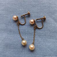 Pair of vintage screwback earrings displayed on fabric, showing gold-tone metal, chain drops, and two pearls on each earring.