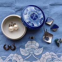 Photo shows all jewelry pieces arranged on blue fabric with lidded blue and white ceramic dish. Includes pearl earrings, silver crescent earrings, cufflinks, ring, and turquoise colored cufflinks.