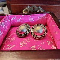 Pair of round domed sterling silver earrings with twisted rope edge, resting in a pink fabric-lined wooden box.
