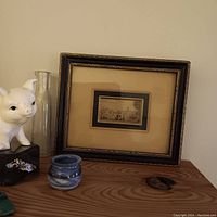 Tiny framed print shown on wooden surface with additional small decorative objects around it, highlighting size and framing.