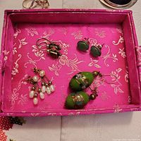 Four pairs of vintage costume earrings arranged on a pink floral fabric tray, showing style and scale.