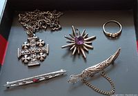 Flat lay of the five pieces of vintage costume jewelry showing cross necklace, amethyst pendant, ring, tie bar brooch, and filigree dagger brooch.