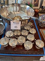 Photo of silver plated punch bowl, 12 matching cups, and large ladle arranged on a wooden table reflecting ambient light
