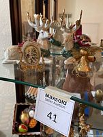 Front view of the Christmas decorative items on glass shelf showing two ceramic reindeer, gold tin angel ornament, and double-sided egg ornament with Santa image.