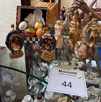 View of two ceramic Nativity scene eggs on gold-tone stands alongside three gold-toned resin angels and one ceramic Christmas girl figurine.