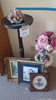 Wood cocktail table with round top, tripod base, dark wood finish, and floral decoration on top, plus framed art on floor nearby