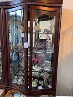 Front view of wood curio cabinet with glass shelves filled with items showing inlayed edged glass doors and large bottom drawer.