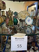 Overview photo of glass shelf with vintage clock, three bejeweled perfume bottles, enamel picture frame, and metal bowl with faux florals.