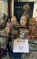 Display of multiple decorative eggs, including Fabergé style music boxes and ceramic egg, alongside a book 'The Imperial Eggs.'