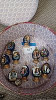 Top-down view of all ten religious Faberge egg ornaments displayed inside the round blue and white damask patterned hat box on carpeted floor.