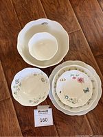 Top-down photo of assorted bowls and plates arranged on a wooden floor showing size variation in serving bowls and plates decorated with Lenox Butterfly Meadow pattern.